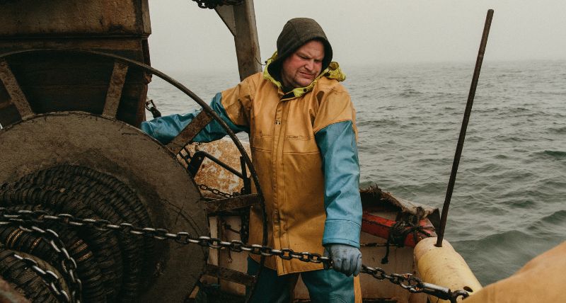 A fisherman at work on deck in full waterproofs hauling in the catch. Copyright Pete Robinso A fisherman at work on deck in full waterproofs hauling in the catch. Copyright Pete Robinson