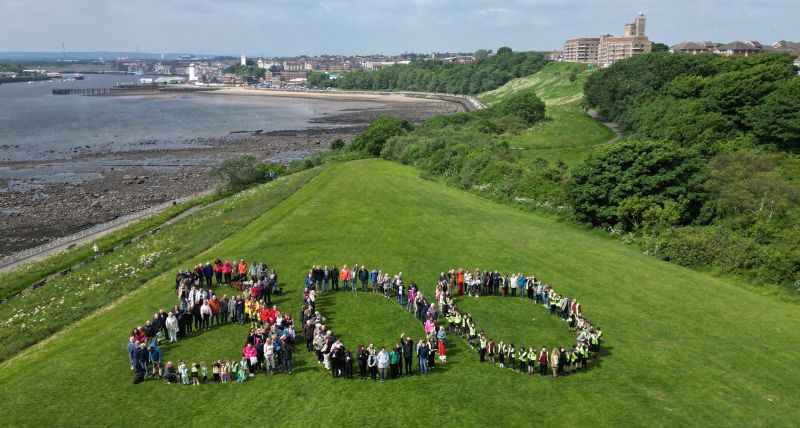 Dozens of people standing in the shape of an 800 on a grassed area with the river behind Dozens of people standing in the shape of an 800 on a grassed area with the river behind