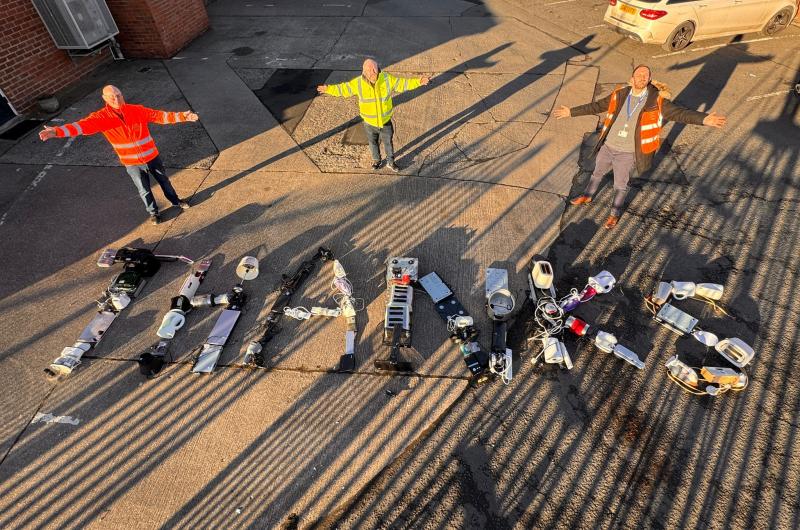 Three men in high visibility clothing standing around the word thanks made out of small electrical items