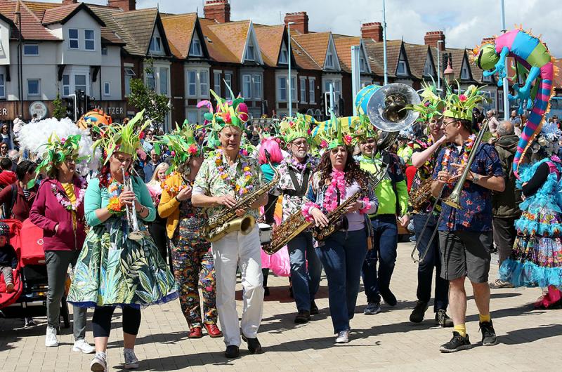 A band of musuicians with trombones and saxophones and dressed in colourful carnival clothes parading through the streets