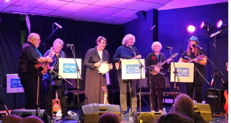 People playing ukeleles on a stage and a woman singing 